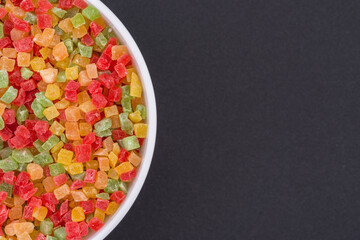 White glass bowl of candied fruit. Isolated on a dark grey background. Top view close up
