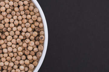 White glass bowl of white pepper. Isolated on a dark grey background. Top view close up