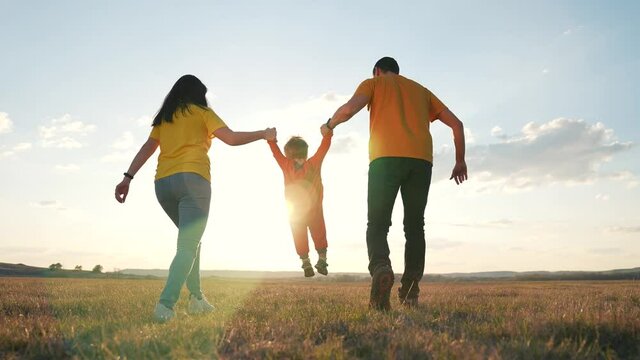 Happy family run in park at sunset. Teamwork. Parents and son are run at sunset. Silhouette of run happy family in park. Family teamwork. Silhouette of happy family in park. Little son smiling