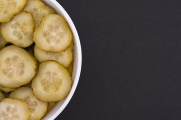 White glass bowl of sliced salted cucumber. Isolated on a dark grey background. Top view close up