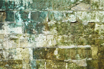 An old wall of gray rectangular blocks, green with age. Texture, background.