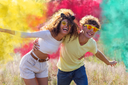 Beautiful young man and woman surrounded colored smoke bombs fog - Happy friends having fun in the park with multicolored smoke bombs - Young students celebrating spring break together. Holi festival.