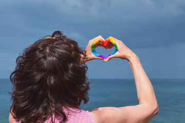 Woman on her back forming a heart with her hands. The heart is painted with the colors of the rainbow.
