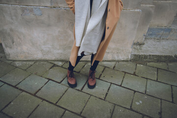 Fototapeta na wymiar legs of a woman, beige cashmere coat, white warm scarf, brown boots for autumn, street fashion