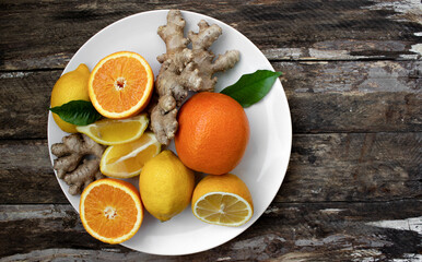 citruses on a white plate, oranges, lemons and ginger on a white plate on wooden background