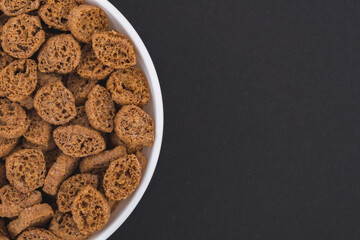 White glass bowl of crispy rye crouton bread biscuits. Isolated on a dark grey background. Top view close up