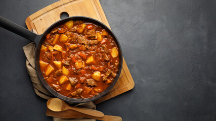 Goulash, beef stew with vegetables in tomato sauce. Top view. Dark (black) background.