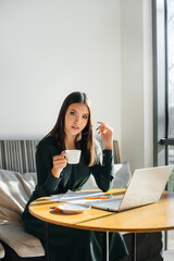 A young beautiful girl is sitting in a cafe, working at a computer and communicating in social networks.