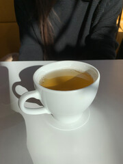 A cup of tea on the table in the rays of the sun. In the background there is a man. Blurred background
