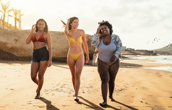 Happy multiracial women with diverse body size having fun walking on the beach during summer holidays