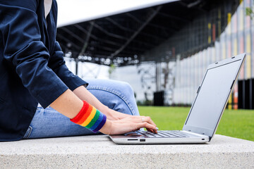 Close-up of woman hands with laptop and LGBT bracelet in modern park . LGBTQIA culture.