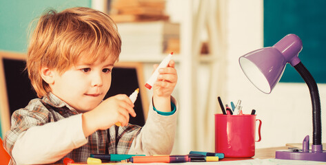 Kid is learning in class on background of blackboard. Happy smiling pupil drawing at the desk. Back to school. Preschooler