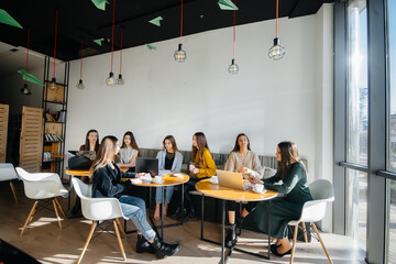 A group of young girls sit in an office at computers and discuss projects. Communication and training online.
