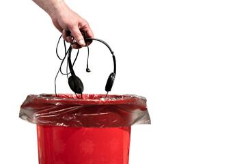 A man throws old wired headphones into the trash can. Male hand throws unnecessary headphones into the trash on a white background close-up.