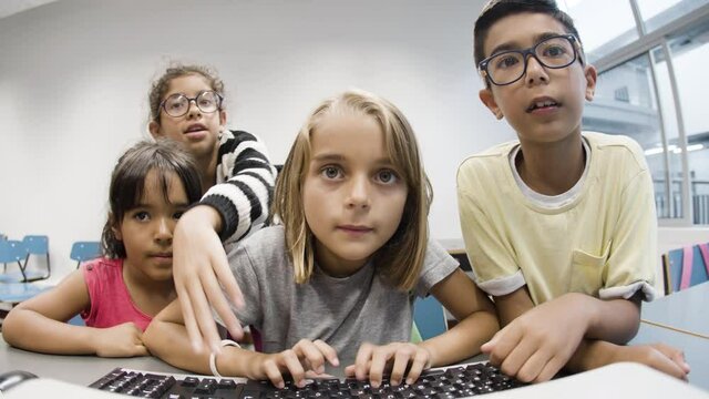 Kids happy with first lesson in computer science after vacation. Multiethnic children sitting at desk, looking at monitor. Excited blonde girl and boy typing. Friendship, digital education concept.