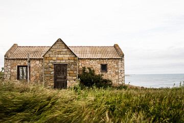 Old abandoned house made of stone by the sea against the background of sky and grass.