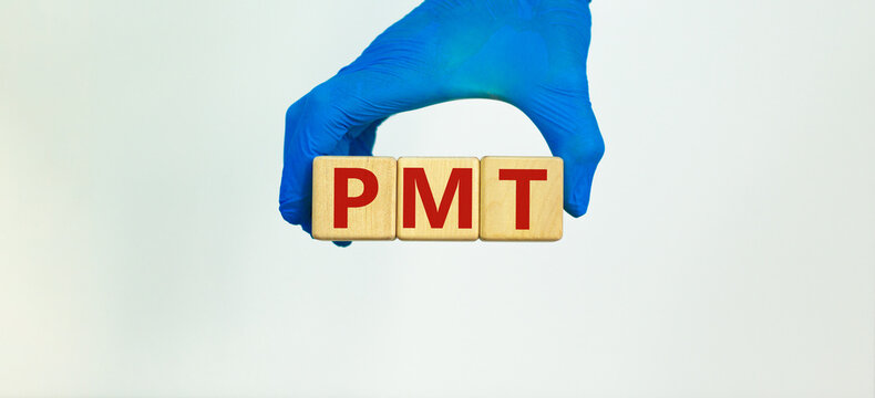Medical and PMT, premenstrual tension symbol. Hand in blue glove holds wooden cubes with the word 'PMT'. Beautiful white background. Medical and PMT, premenstrual tension concept. Copy space.