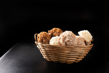 Cocada, Coconut candy from Brazil, white and brown cocadas in a straw basket on dark surface, black background, selective focus.