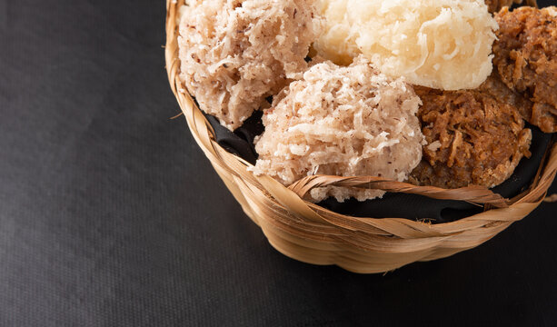 Cocada, Coconut candy from Brazil, white and brown cocadas in a straw basket on dark surface, black background, selective focus.