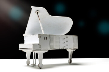 Decorative toy white grand piano on a white surface with dark background