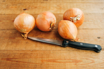 Four beautiful golden onion bulbs on a wooden background. Cooking. The knife is on the table.