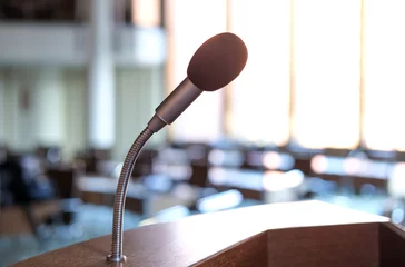 Fototapeten Konzept Kommunikation: Leerer Konferenzsaal oder Sitzungsraum mit Fokus auf das Mikrofon des Rednerpultes im Gegenlicht © redaktion93