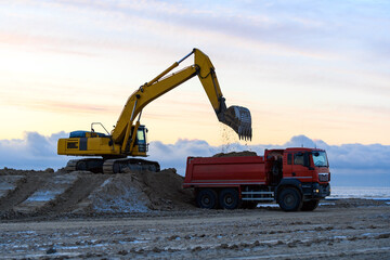Fototapeta na wymiar Yellow excavator loads ground into the dumper. The road construction.