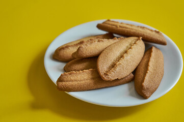 Baked cookies on white plate on yellow background.
