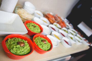 Red bowls with smashed avocado and white bowls with other ingredients for burgers (mayo, ketchup, mustard, tomato, pickles, onion)