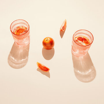 Bloody oranges and glasses of fresh lemonade or water on on pastel beige backgound. Summer refreshment concept. Sunlit flat lay. Minimal style. Top view