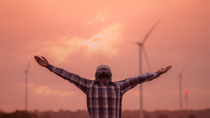 Fototapeta na wymiar African engineer windmills wearing white hard hat standing with wind turbine on silhouette sunset