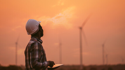African engineer windmills wearing white hard hat and using tablet with   wind turbine on...
