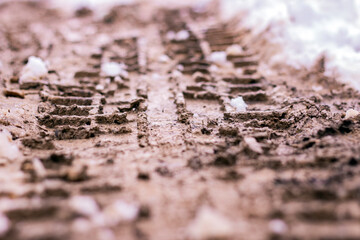 Wheel tracks on mud and snow. Snow on dirty soil with car wheel tracks. Dirty melting snow on the road. Selective focus with blurred background.