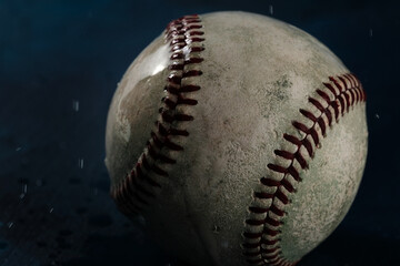Dark wet baseball covered in water for game rain delay concept, close up color view of old used ball on background.