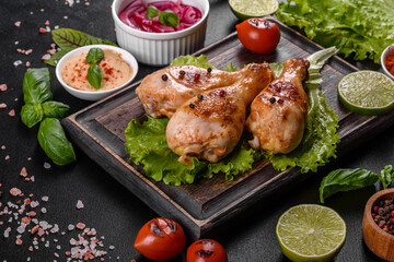 Tasty grilled chicken legs with spices and herbs on a wooden board on a dark concrete background