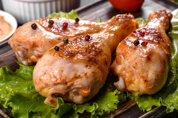 Tasty grilled chicken legs with spices and herbs on a wooden board on a dark concrete background