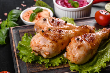 Tasty grilled chicken legs with spices and herbs on a wooden board on a dark concrete background
