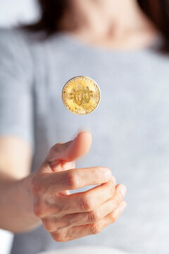 a woman is flipping a coin using a bright colored bitcoin. A concept image for investing in crypto currency and its risky uncertain nature. It can go up or down similar to the odds of a coin toss.