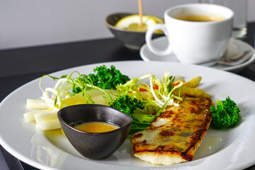 on a black table a white plate with dinner, fried fish with fresh vegetables