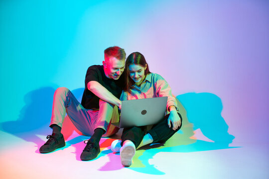 Modern young couple girl and guy working on laptop or shopping online. Colored neon studio light