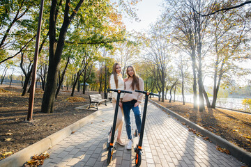 Two young beautiful girls ride electric scooters in the Park on a warm autumn day