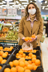 A woman in a medical mask and gloves choose oranges in the supermarket. Shopping during the coronavirus lockdown. Epidemic of Covid-19 Restriction Concept