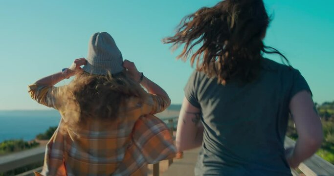 Handheld authentic and real POV shot of friends running together at sunset wooden boardwalk. Happy teenage freedom vibes, summertime lifestyle of travel millennials. Female support and friendship