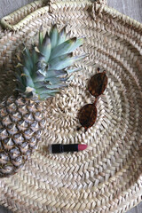 Straw bag, sunglasses, lipstick and pineapple on wooden background. Flat lay.