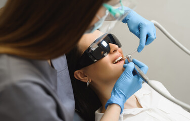 First person close-up shot of a dentist treating teeth of a young woman. The doctor drilling the teeth to eliminate caries and place a filling after.