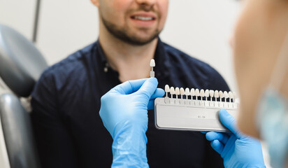 Young woman dentist selecting a shade of enamel for implantation. Male patient consults on dental...