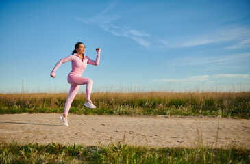 Young sporty woman in pink sportswear running outdoors on a beautiful sunny early summer day