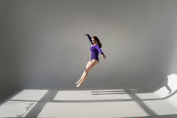 Sexy plus size model with big breasts in purple bodysuit jumping in studio