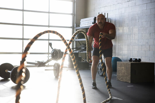 Strong man doing battle rope exercise in sunny cross training gym
