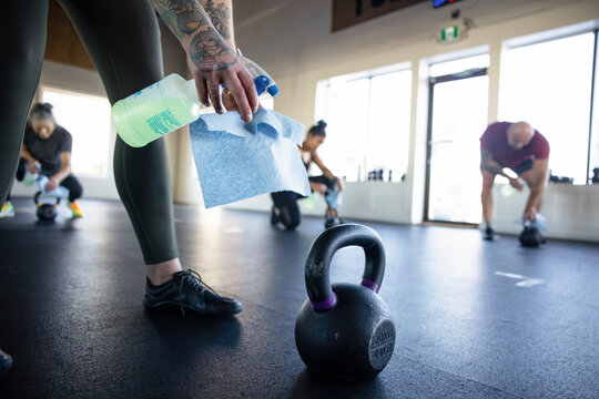 Woman disinfecting kettle bell with spray cleaner in gym studio
